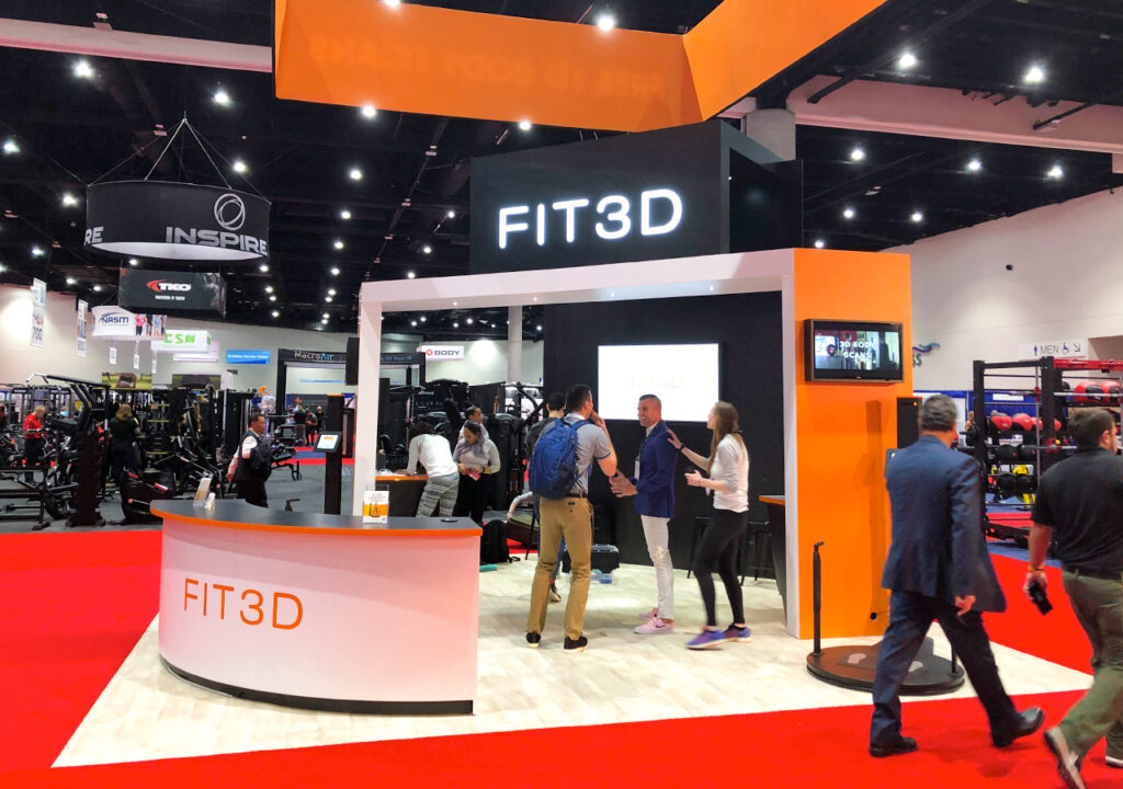 FIT3D trade show booth with orange branding and attendee interaction