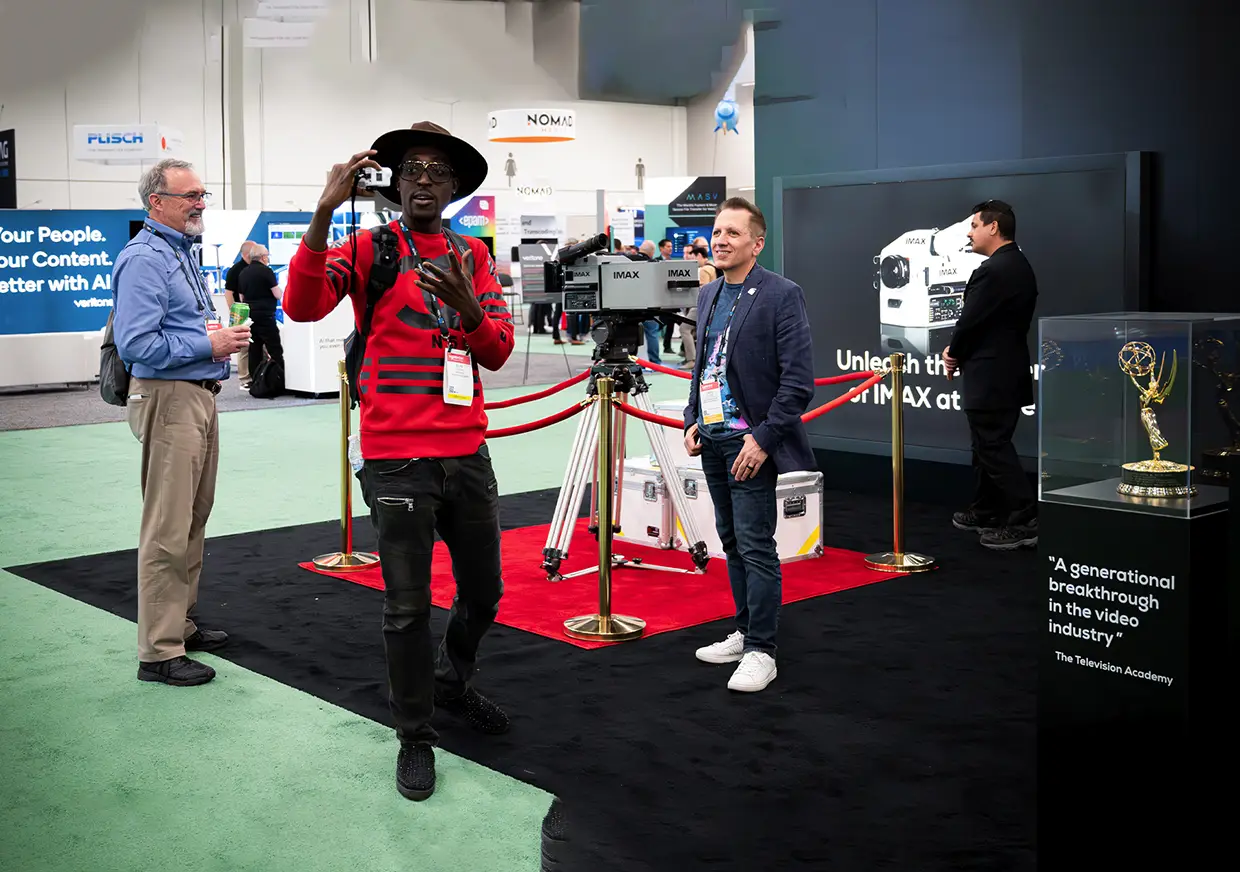 Presenter speaking beside demonstration equipment at IMAX Enhanced trade show booth