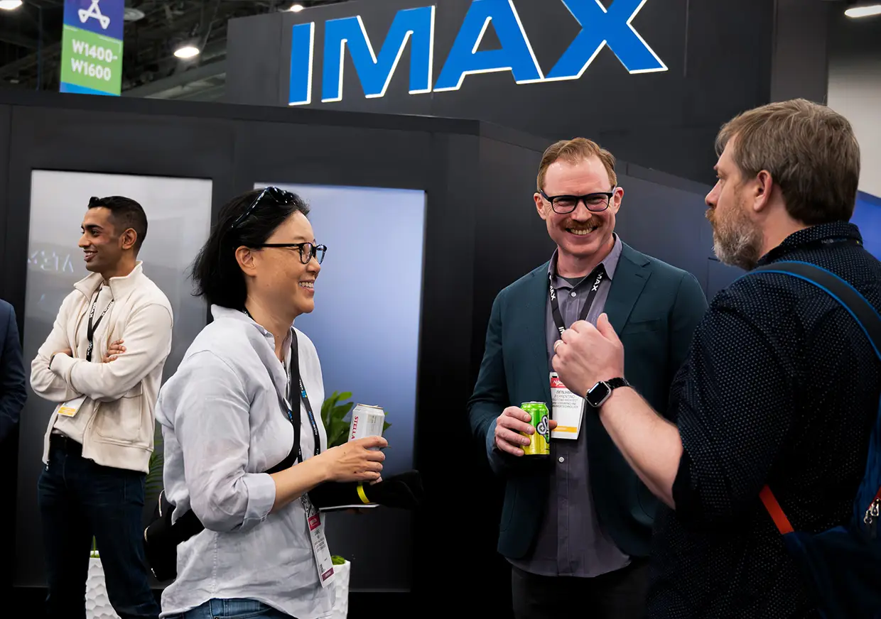 Trade show attendees networking beneath large illuminated IMAX booth signage
