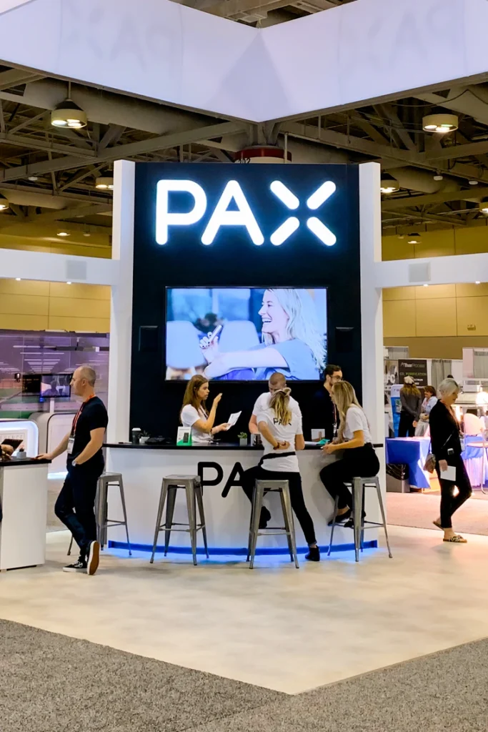 PAX branded trade show booth with central screen and visitor seating
